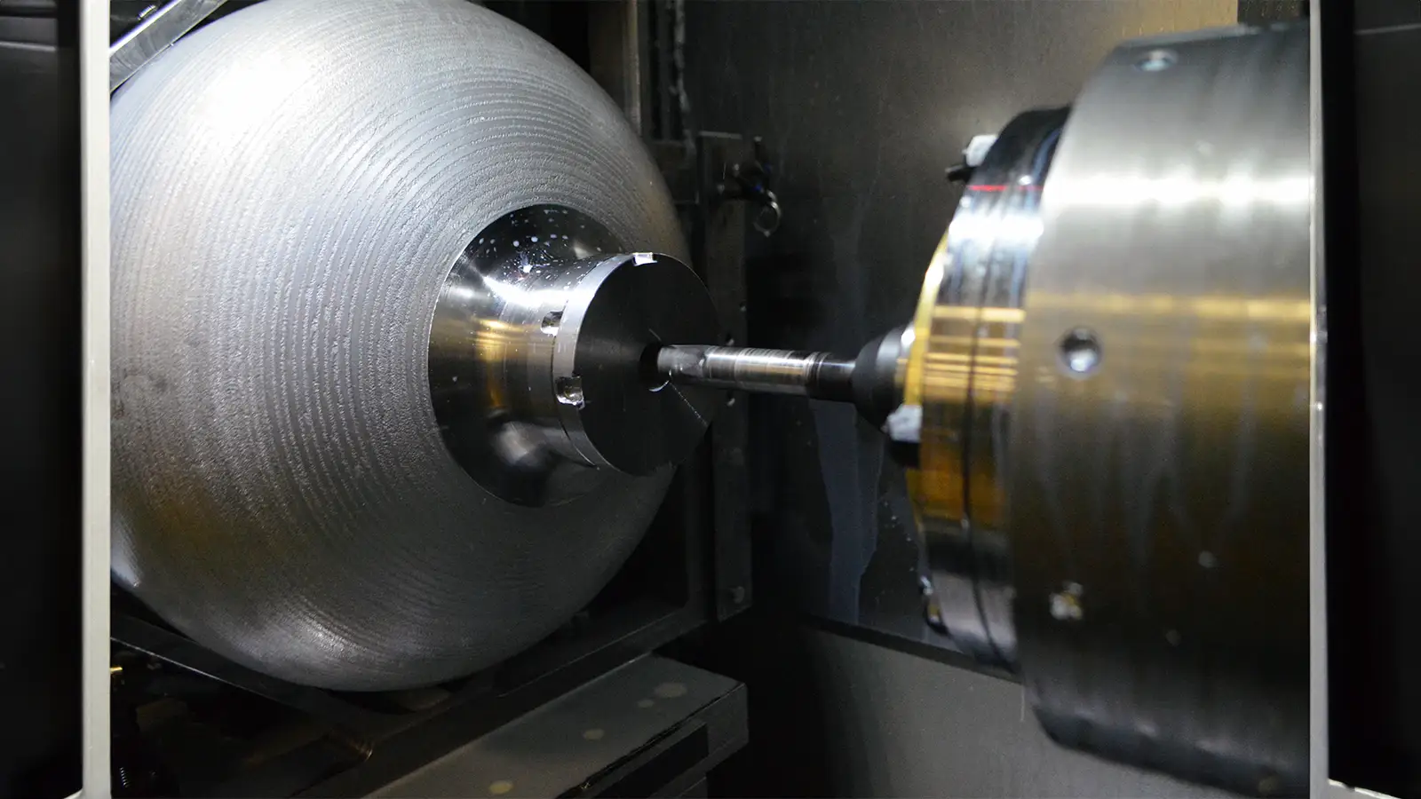 Image closely capturing the machining of a metal cylinder inside a CNC machine.