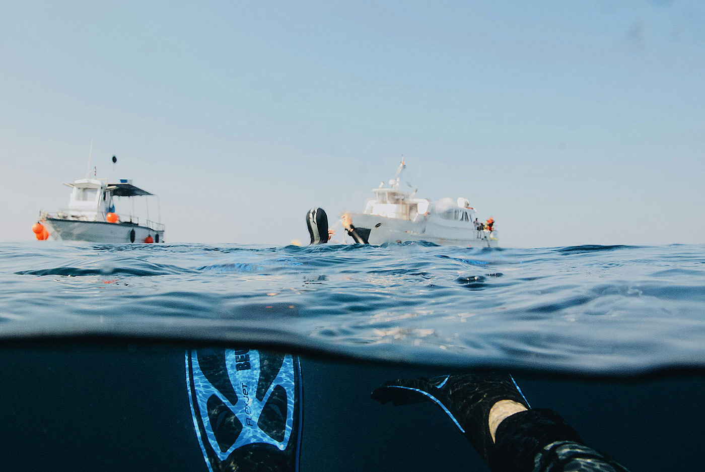 Diver surfacing near dive boats in open water, representing Steelhead’s lightweight composite pressure vessels used in the Avelo Dive System for enhanced underwater mobility, buoyancy control, and diver comfort.