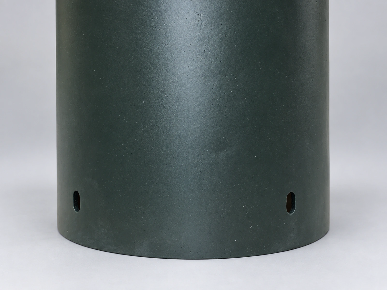 Studio close-up of the green-gray composite tube surface and two oval openings near its lower edge.