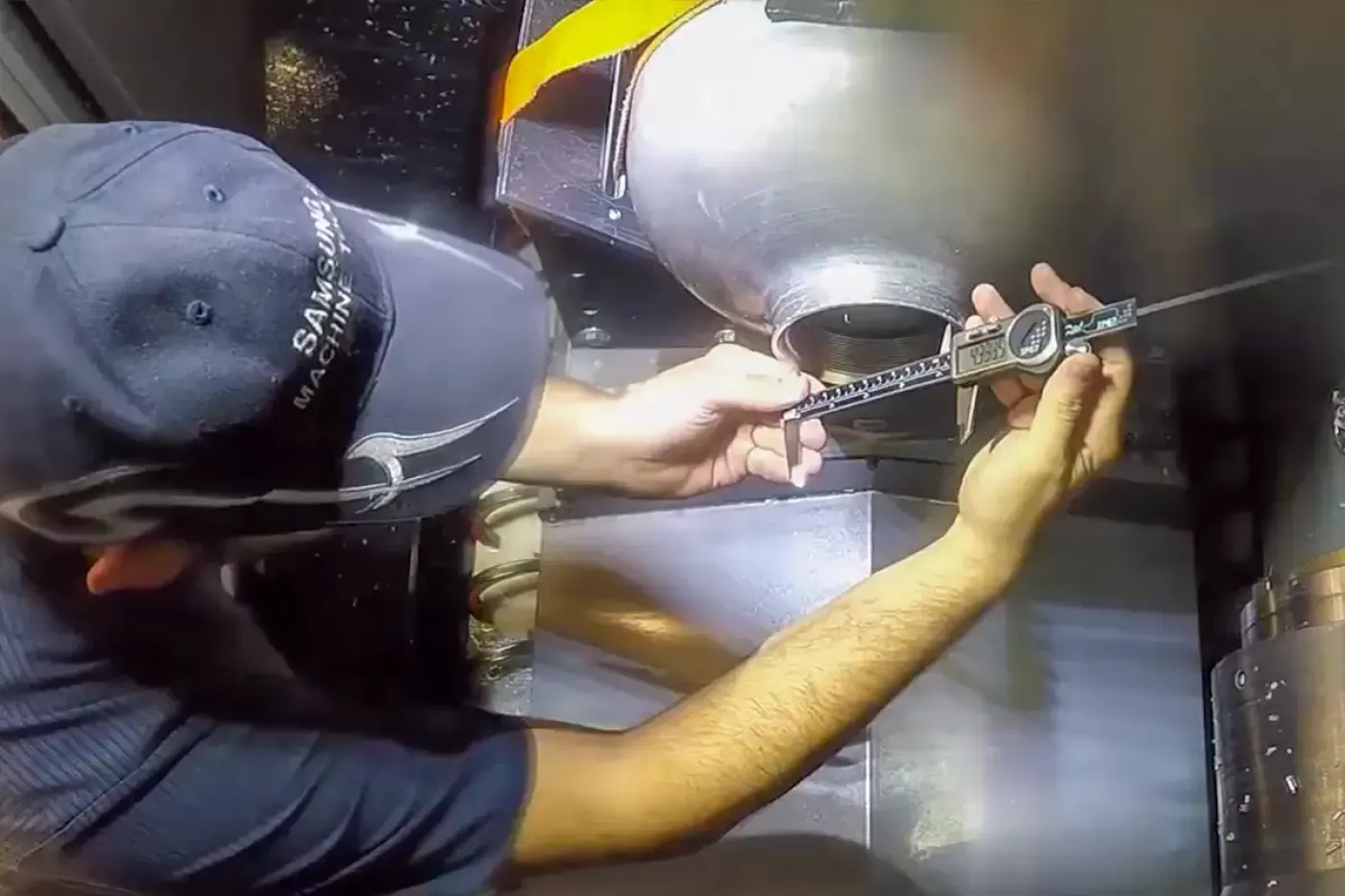  image depicting a technician using a digital caliper to measure a precision-machined metal cylinder within a CNC machine environment.