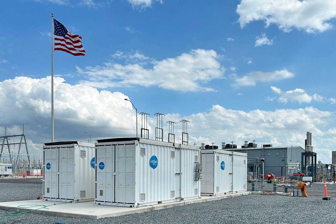 Steelhead ground-mounted composite pressure-vessel storage modules deployed at an industrial energy site, showing stationary high-capacity gas and hydrogen storage containers integrated with facility infrastructure, with vent stacks and utility connections visible under a partly cloudy sky.