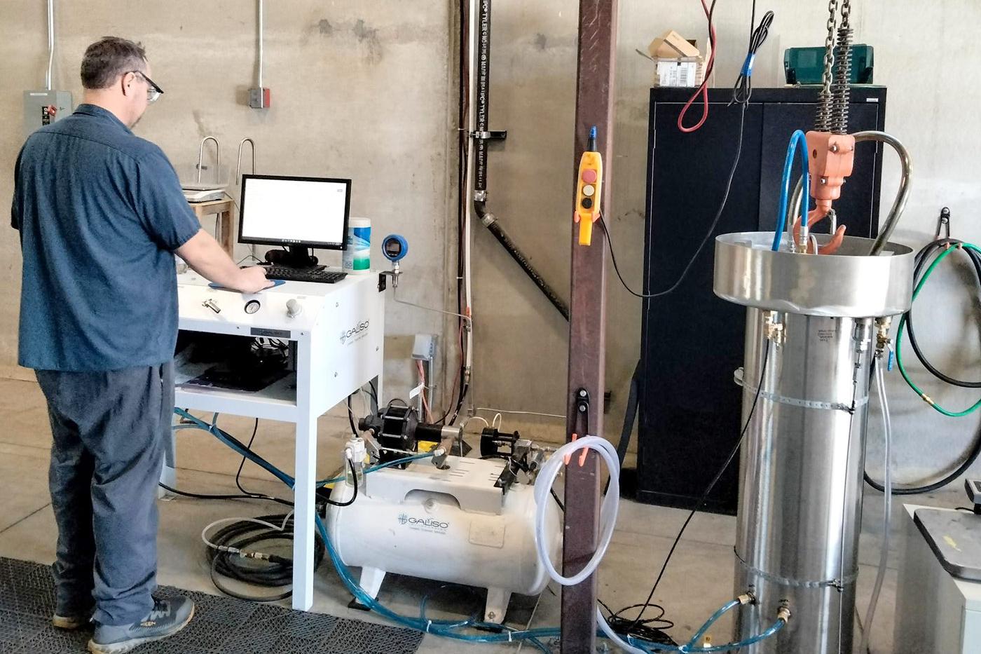 Technician operating testing equipment beside a pressure vessel in Steelhead’s Golden, Colorado facility, representing 100% U.S.-made Type 3 and Type 4 composite vessels built with full quality control and Buy America compliance.
