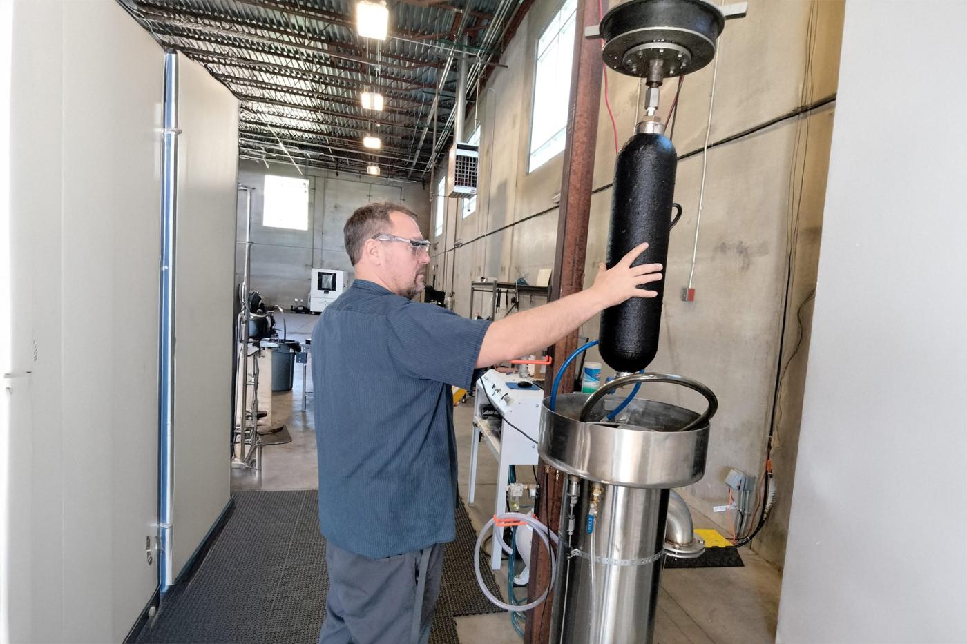 Technician loading a composite pressure vessel into a water-jacket proof-testing chamber inside a manufacturing test facility, preparing the cylinder for hydrostatic validation as part of certification and performance verification.