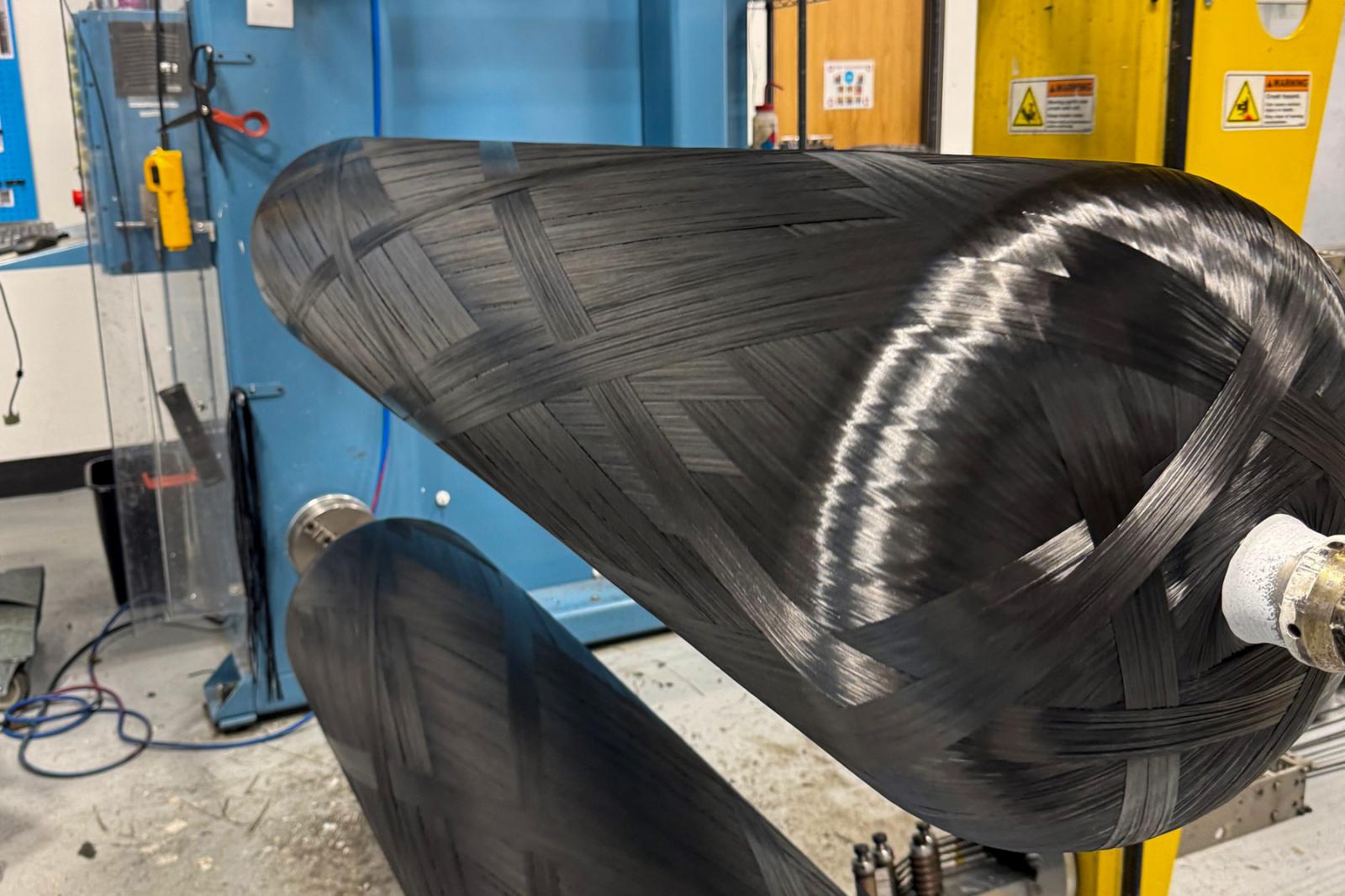 Carbon fiber being filament wound onto a Type 4 CNG pressure vessel on a manufacturing machine in a production facility.