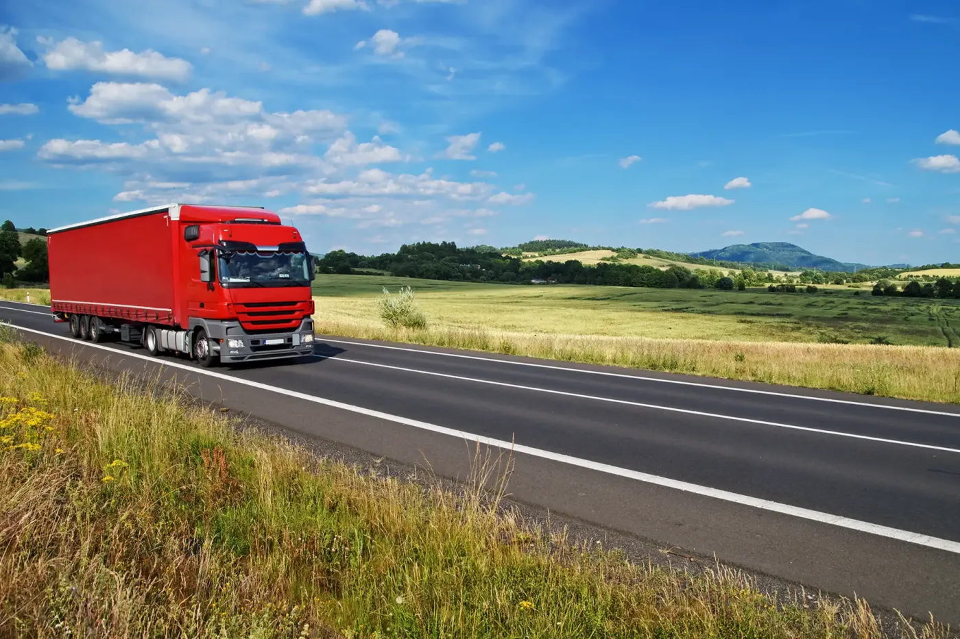 Red heavy-duty truck driving on a highway, representing the use of lightweight CNG cylinders in commercial vehicles to enhance fuel efficiency and maintain performance.
