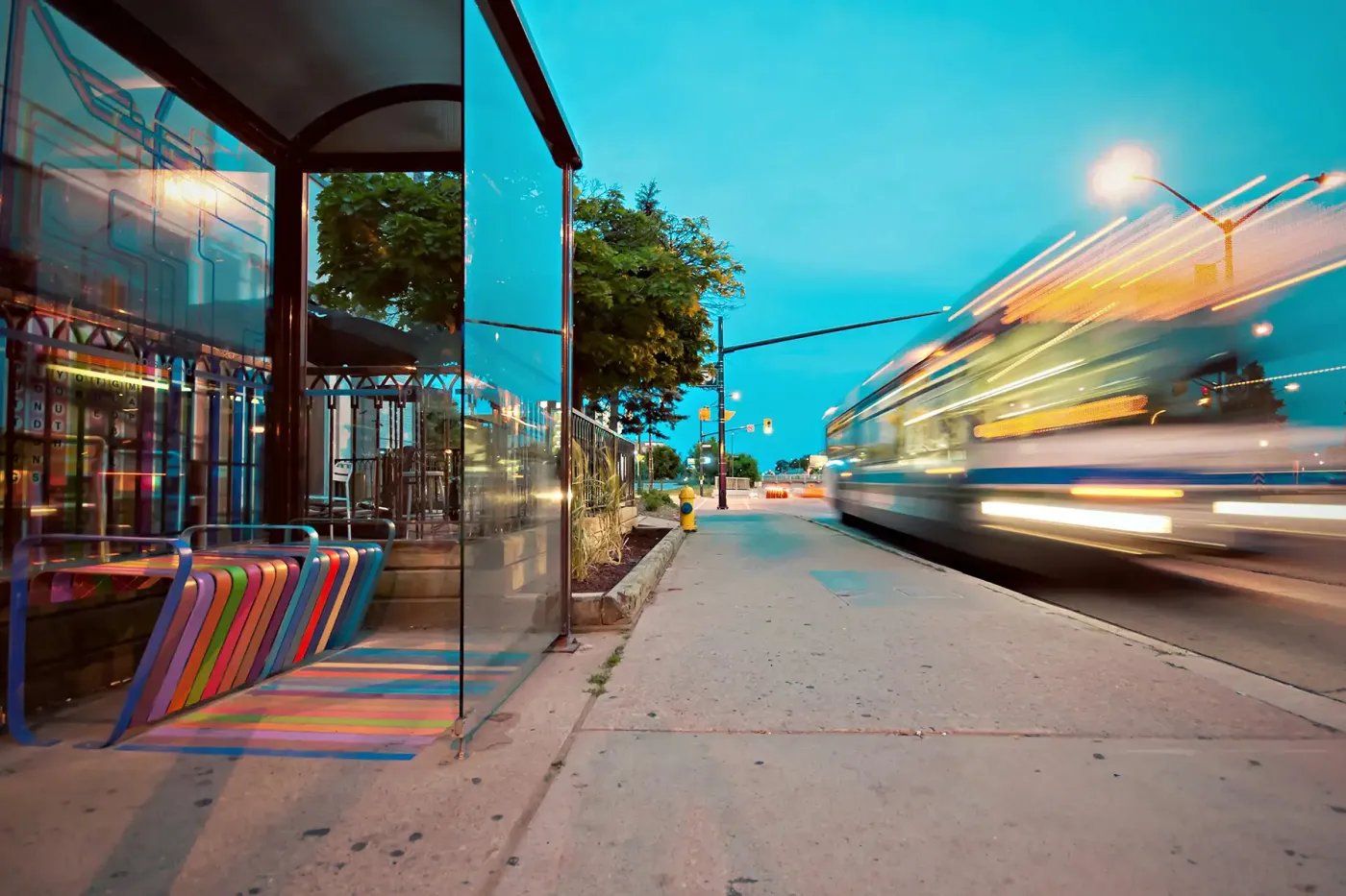 Blurred motion of a city bus pulling up to a bus stop at dusk, symbolizing the adoption of CNG fuel systems for transit fleets to reduce emissions and operating costs.